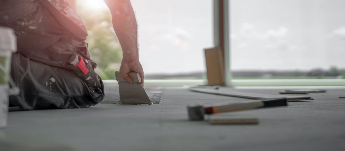 Handwerker verteilt den Parkettkleber mit der Kleberspachtel auf dem frischen Estrich beim Parkett legen